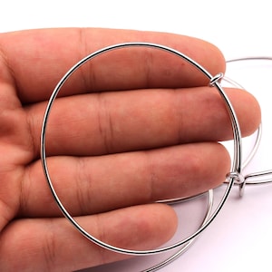May include: Three silver-coloured, adjustable bangle bracelets. The bracelets are round and made of thin metal. The adjustable mechanism is visible on each bracelet. The background is white.
