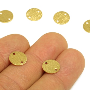 May include: Close-up of several small, round, gold-coloured metal jewellery components. Each component has a textured surface and two or three small holes. The components are shown against a white background.