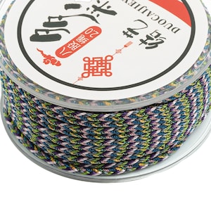 Puede incluir: Una bobina de cordón trenzado multicolor con una etiqueta blanca que dice "Duocaliber #2 20"