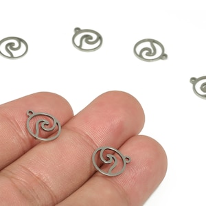 Può includere: Piccoli ciondoli a forma di onda color argento con un anello per la creazione di gioielli. I ciondoli hanno la forma di un'onda all'interno di un cerchio. Diversi ciondoli sono sparsi su sfondo bianco.