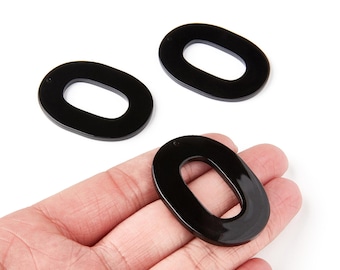 May include: Three glossy black oval-shaped acrylic beads. One bead is held in a hand, with two others scattered nearby. The beads have a smooth, polished finish and a hole at the top for stringing.
