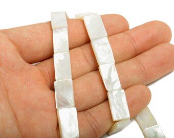 May include: Strands of rectangular, iridescent white mother-of-pearl beads. The beads are held in a hand, showcasing their smooth, polished surface and natural variations in color. Ideal for jewelry making.