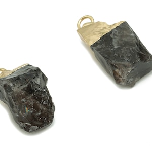 May include: Two black gemstone pendants with gold accents. The gemstones are rough and have a natural, irregular shape. The gold accents are on the top of the pendants and are in the shape of a loop.