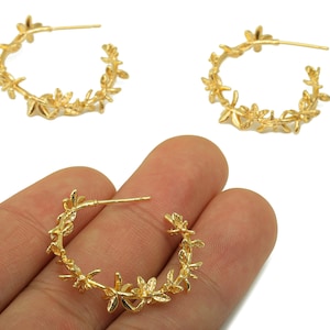 May include: Gold-coloured hoop earrings featuring a floral design. The earrings are decorated with small, detailed flowers and leaves, creating a delicate and elegant appearance. The earrings are shown on a white background.