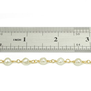 May include: A close-up of a pearl necklace with gold wire accents. The necklace is measured against a ruler, showing it is approximately 3 inches long.