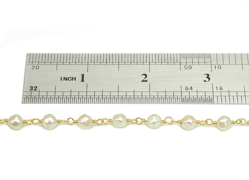 May include: A close-up of a pearl necklace with gold wire accents. The necklace is measured against a ruler, showing it is approximately 3 inches long.