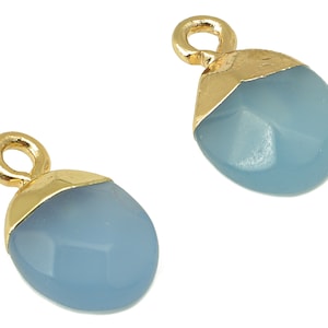 May include: Two blue teardrop-shaped pendants with gold-colored caps and loops. The pendants have a faceted surface and a light blue color. The gold caps add a touch of elegance to the jewelry.