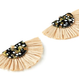 May include: A pair of black and white patterned earrings with a beige fringe. The earrings are shaped like a half-circle.