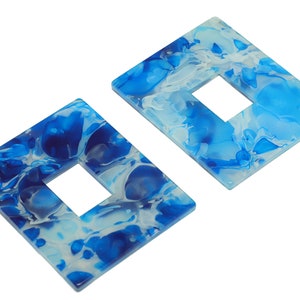 Puede incluir: Dos pendientes de forma cuadrada con un diseño marmoleado azul y blanco. Los pendientes tienen un agujero cuadrado en el centro.