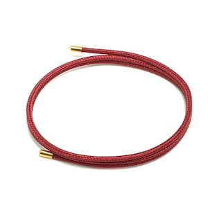 May include: A red braided cord with gold-coloured ends. The cord is coiled into a circle.