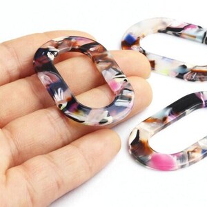 Peut inclure: Liens ovales en acrylique avec un motif marbré noir, blanc, rose et violet. Les liens à centre ouvert sont probablement des composants de bijoux ou des éléments décoratifs. Les liens sont présentés sur un fond neutre.