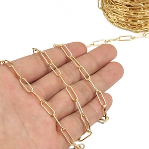 May include: A gold chain made of oval-shaped links. The chain is lying on a hand.