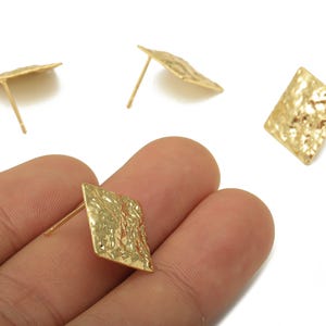 May include: Gold-colored, textured square stud earrings. The earrings have a hammered metal appearance and are shown on a white background. The earrings are a geometric shape and are a jewelry item.