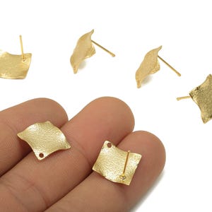 May include: Gold-toned, textured square stud earrings with a post backing. The earrings have a slightly wavy, organic shape. Several earrings are displayed on a white background, with two held in a hand.