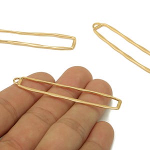 May include: Gold-colored rectangular jewelry findings with a textured, hammered appearance. The findings have a loop at one end for attaching to other components. The image shows several of these findings, ideal for jewelry making.
