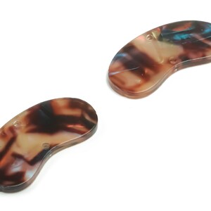 May include: Two brown and white tortoiseshell plastic hair clips in the shape of a bean.