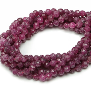 May include: A strand of faceted ruby beads, each bead is a deep red color and has a faceted finish. The beads are strung together on a clear thread.