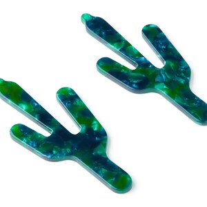 May include: Two green and blue cactus-shaped hair clips. The clips are made of a marbled plastic material.