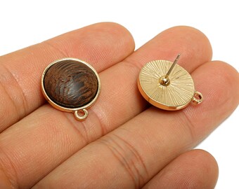 May include: Two round stud earrings. Each earring features a dark brown, wood-like center set in a gold-colored bezel. The back of one earring shows the post and a textured design. Both earrings have a small loop for attaching a charm.