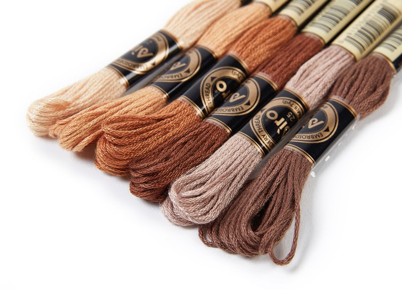May include: Six spools of embroidery floss in shades of brown, beige, and peach. The spools are labeled "Silo Embroidery Thread" and feature a gold logo.