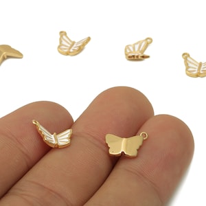Puede incluir: Encantos de mariposa dorados con detalles de esmalte blanco. Los amuletos están en varias poses, algunos con un lazo para sujetarlos a la joyería. Estos amuletos pequeños y delicados son perfectos para proyectos de manualidades.