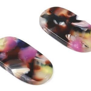 May include: Two oval-shaped, multi-coloured, resin hair clips. The clips have a mottled pattern of black, brown, pink, yellow, and white.