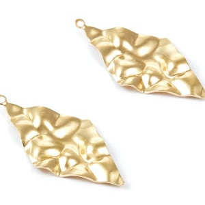 Op de afbeelding: Twee gouden metalen oorbellen met een getextureerd, golvend, bladvormig ontwerp. Elke oorbel heeft een kleine lus aan de bovenkant om aan een haak te bevestigen.