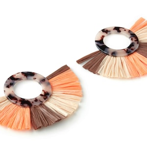 May include: A pair of earrings featuring a tortoiseshell-patterned circle and a fringe of brown, beige, and orange tassels.