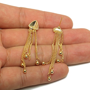 May include: A pair of gold-colored dangle earrings. Each earring features a geometric top with multiple delicate chains. Small, round beads are attached to the ends of the chains, creating a flowing, elegant design. The earrings are displayed against a white background.
