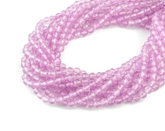 Può includere: Un filo di perline di vetro sfaccettate rosa chiaro. Le perline sono rotonde e hanno una forma leggermente irregolare. Le perline sono infilate su un filo trasparente.