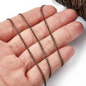 May include: A close-up of a black and copper chain, with a slightly textured finish. The chain is coiled and laid out on a hand, showing the length and detail of the chain.
