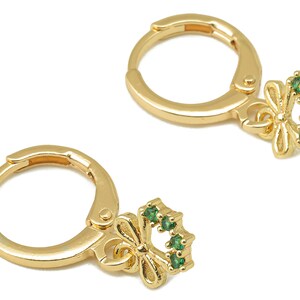以下が含まれることがあります： 緑色の石の弓形のチャームが付いた、金のフープピアス。弓形のチャームは、緑色の石の円形に囲まれています。