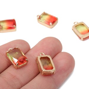 May include: Rectangular gemstone pendants with a gold-colored frame. The gemstones have a gradient of colors, transitioning from red to yellow. Each pendant has a small loop for attaching to jewelry.
