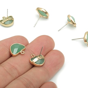 May include: A collection of gold-toned stud earrings with a light green, heart-shaped stone. The earrings have a post and a small loop on the back. The earrings are displayed on a white surface.