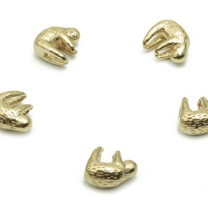 May include: Five gold-colored sloth charms, each with a different pose, are arranged in a circle on a white background.