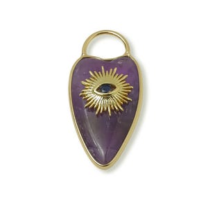 May include: A gold-toned pendant with a purple, heart-shaped amethyst stone. The pendant features a gold sunburst design with a blue eye in the center. The pendant has a small loop at the top for a chain.
