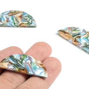 May include: Three half-circle beads with a marbled pattern in blue, green, tan, and white. One bead is held in a hand. These beads are likely for jewellery making or crafting.