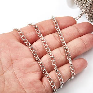 May include: A silver curb chain, also known as a Cuban chain, is shown in a hand. The chain is made of metal links that are interlocked in a pattern. The chain is a popular choice for jewellery and accessories.