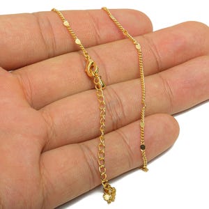 May include: A delicate gold-colored necklace with a small chain and circular accents. The necklace has an adjustable length and a lobster clasp closure. The jewelry is displayed against a neutral background.
