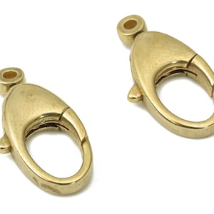 Puede incluir: Dos cierres de langosta de metal dorado, cada uno con una abertura de resorte y un bucle ovalado liso.