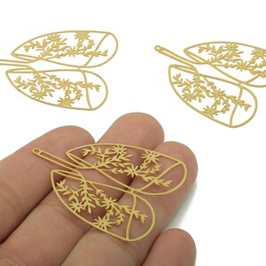 May include: Gold-coloured metal leaf-shaped charms with floral cutouts. The charms have a delicate, openwork design featuring detailed floral and leaf patterns. These charms are ideal for jewellery making or craft projects.