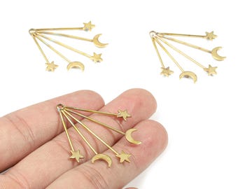 May include: Gold-colored celestial charms featuring a crescent moon and star design. Each charm has a series of thin, radiating lines. The charms are shown on a white background and in a person's hand.