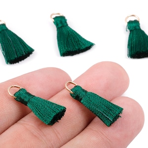 May include: Close-up of several dark green tassels with gold-colored loops. The tassels are made of silky threads and are displayed against a white background. These decorative tassels are ideal for jewelry making or craft projects.
