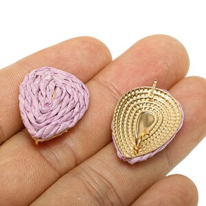May include: Two lavender-coloured, woven raffia earrings. One earring is whole, the other shows the gold-coloured back with a post. The earrings are teardrop-shaped and have a gold-coloured base.