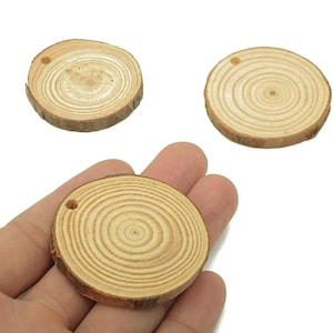 May include: Three small, round wooden slices with a natural wood grain pattern. Each slice has a small hole drilled near the edge. One slice is being held in a hand. These wood slices are perfect for crafting.