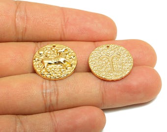 May include: Two gold-colored round pendants. One pendant features a detailed image of a ram, stars, and a crescent moon. The other pendant has the Aries zodiac symbol. Both pendants have a textured surface and a small hole at the top.