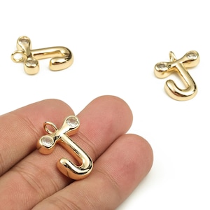 以下が含まれることがあります： 透明なクリスタルアクセントが付いた、金色の金属製の文字「J」チャーム。 チャームは筆記体で、ジュエリーに取り付けるためのループが上部にあります。 1つのチャームは手に持たれ、他の2つは白い背景にあります。