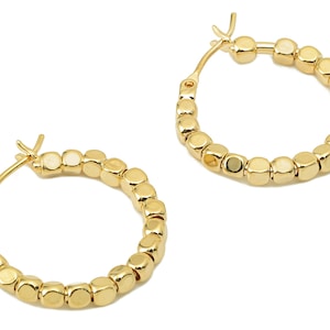 Può includere: Un paio di orecchini a cerchio dorati con un design a perline. Ogni orecchino è composto da piccole perline rotonde dorate.