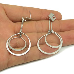 May include: Silver double circle earrings with a simple design. The earrings are made of two circles, one slightly larger than the other, that are connected at the top. The earrings are hanging from a silver post.