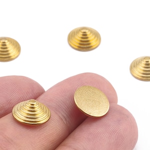 May include: Close-up of several small, gold-colored metal beads. Some beads have a spiral design, while others are flat. The beads are held in a person's hand against a white background. These beads are suitable for jewelry making.